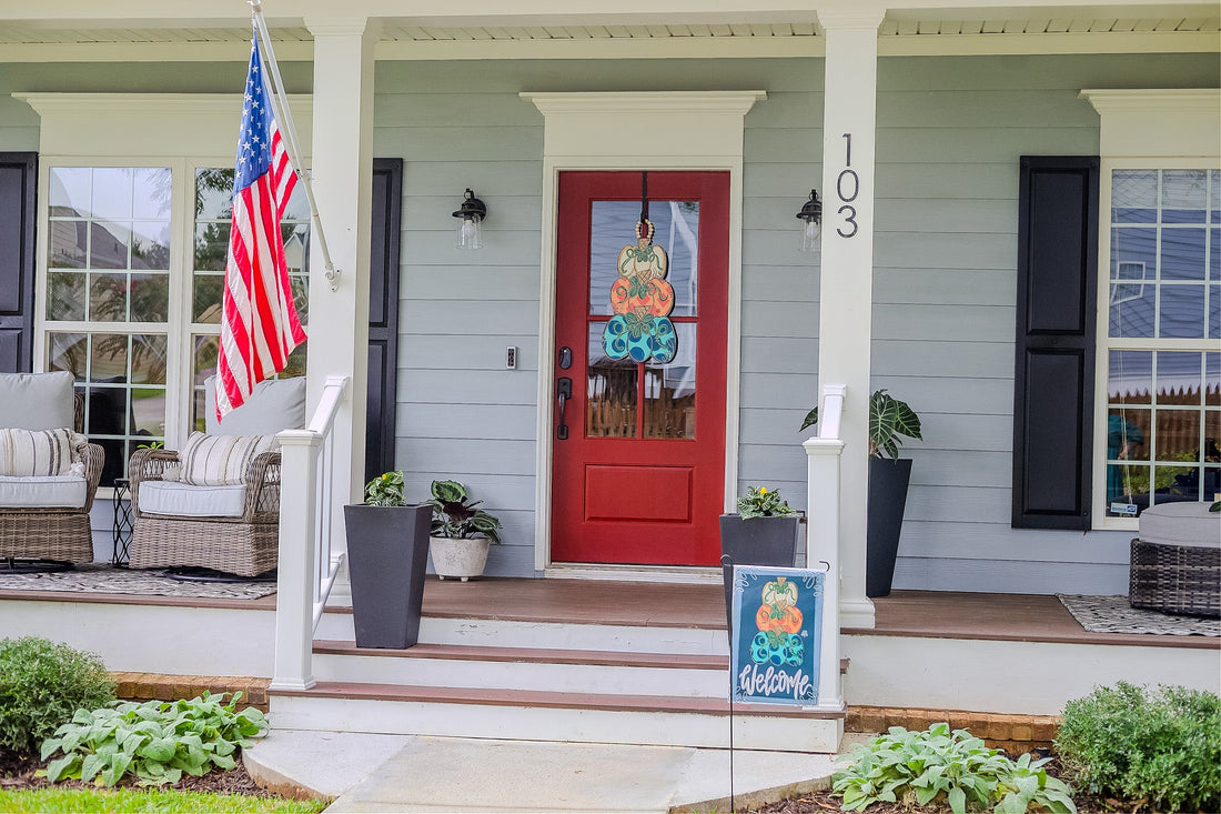 Pumpkin stack door hanger on a red front door with a matching pumpkin stack Welcome Garden Glam by the porch steps